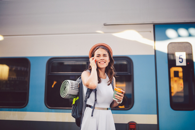 Junge Frau mit Handy auf dem Bahnsteig mit Zug im Hintergrund