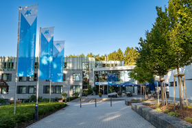 Weg vom Parkplatz zum Eingang des Bildungszentrums mit Bäumen auf der rechten und blauen Arbeitskammer-Fahnen auf der linken Seite