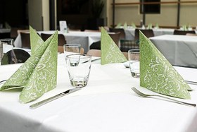 Mit weißem Tischtuch und grünen aufgestellten Servietten gedeckter Tisch im Restaurant des Bildungszentrums