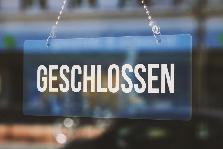Transparentes Schild mit dem Schriftzug "Geschlossen" vor einer Glastür