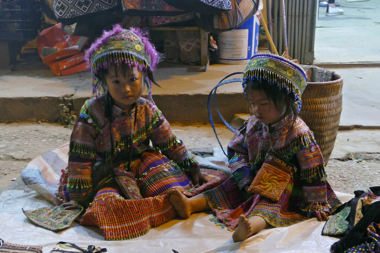 Zwei Kinder in traditionellen Kleidern sitzend auf einem hellen Teppich