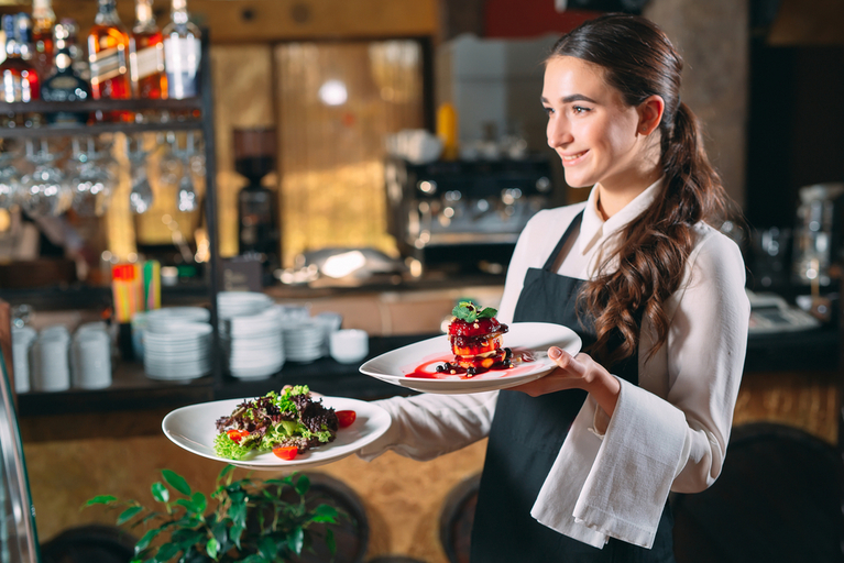 Foto einer jungen Frau, die in einem Restaurant zwei Teller mit Essen zum Tisch trägt