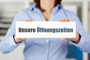 Frau mit einem Schild, auf dem "Unsere Öffnungszeiten" steht