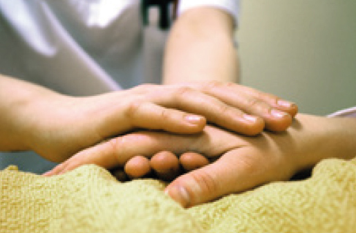 Foto, das die Hand einer Krankenschwester auf der Hand eines im Bett liegenden Patienten zeigt