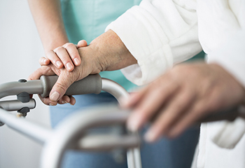 Das Foto zeigt die Hand einer Krankenpflegerin, die sich auf die Hand einer älteren Person am Rollator legt